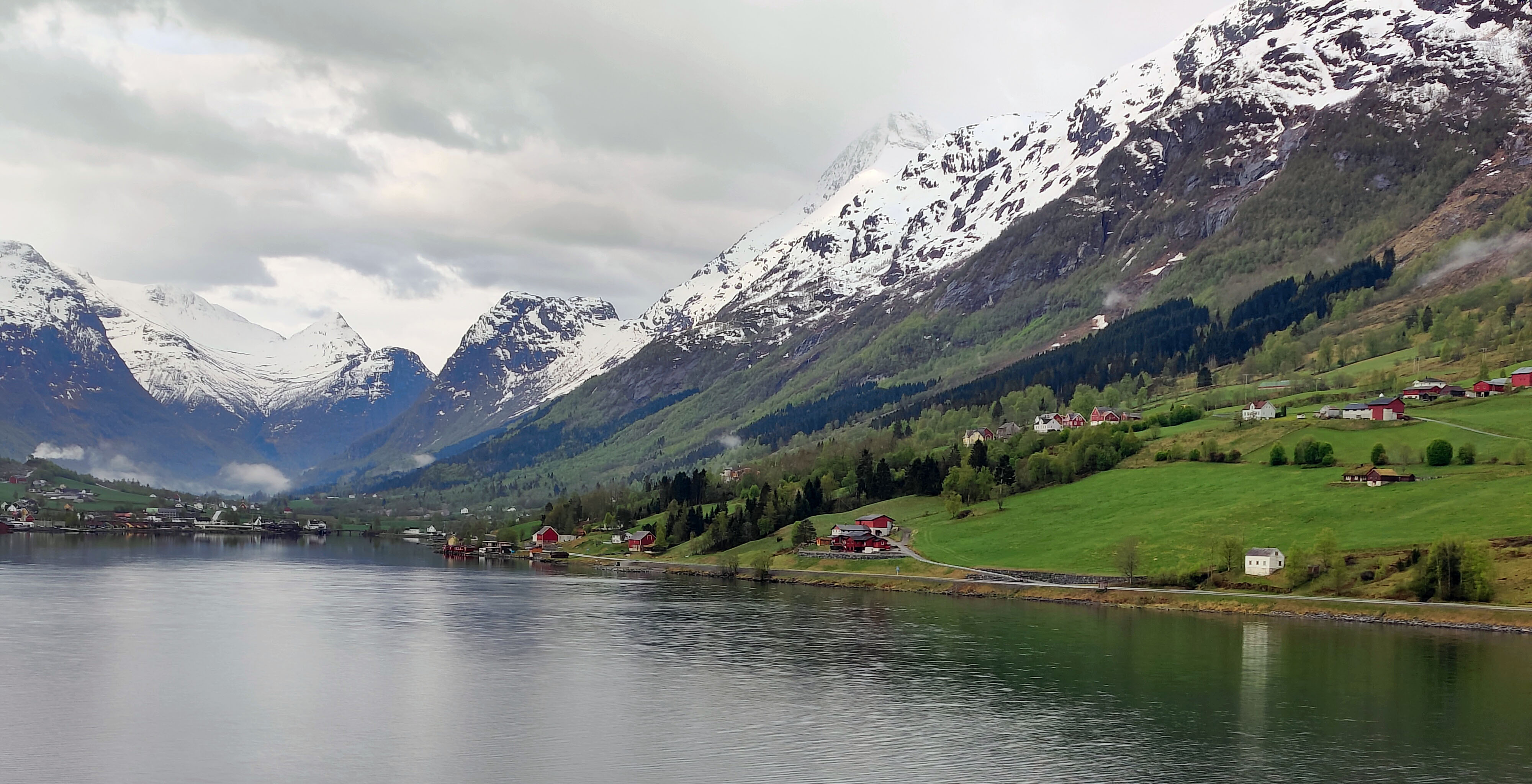 Norwegian fjord with snow covered mountains green fields and red houses